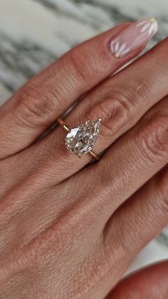 a woman's hand with a pink manicured nail polish and an oval shaped diamond ring