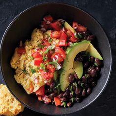 a bowl filled with black beans, avocado and tomato salad next to a biscuit