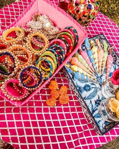 an assortment of bracelets and other jewelry on a pink tablecloth with flowers in the background