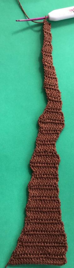 a crocheted piece of brown yarn next to a toothbrush on a green surface