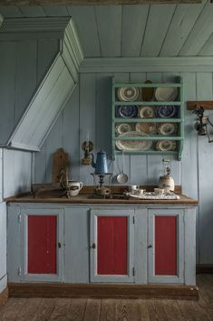 an old fashioned kitchen with blue walls and red cupboards in the center, along with dishes on shelves