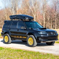 a black suv with yellow wheels parked on a dirt road in front of some trees