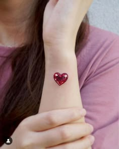 a woman wearing a red heart tattoo on her wrist