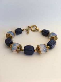 "7.5\"-- 20mm Retangular lapis lazuli gemstone beads and 12mm Opalite Stone beads beautiful statement bracelet, ornate with 15mm brass gold flower caps and a 20mm toggle clasp closure. Hand made jewelry. All purchase will arrive in gifts boxes. Thanks for stopping by!" Blue Moonstone Beaded Bracelets With Gemstone Beads, Handmade Blue Moonstone Beaded Bracelets, Handmade Blue Moonstone Bracelets, Sapphire Lapis Lazuli Beaded Bracelet With Natural Stones, Opalite Bracelet, Chakra Stones Jewelry, Bracelet Weaving, Stone Bead Jewelry, Beautiful Beaded Jewelry