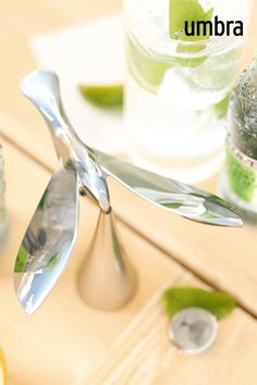 a bottle opener and spoon sitting on top of a wooden table next to two glass bottles