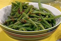 a bowl filled with green beans sitting on top of a yellow tablecloth covered table