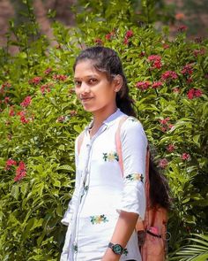 a young woman standing in front of some bushes and flowers with her hand on her hip