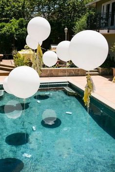 balloons floating in the air over a swimming pool with clear blue water and greenery