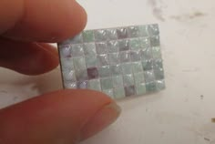 a person is holding a small square shaped object in their left hand and it appears to be made out of glass tiles