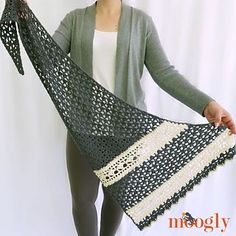 a woman holding up a black and white crocheted shawl in front of a white background