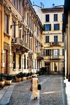 a woman walking down a cobblestone street in an old european city with tall buildings