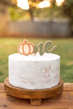 a white cake topped with a wooden one and two pumpkins sitting on top of it