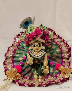 a statue of a woman in green and pink with a peacock on her head, sitting next to a white backdrop