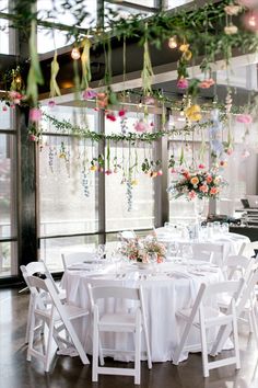 a table with white chairs and flowers hanging from the ceiling