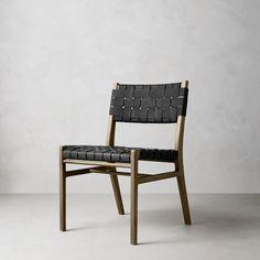 a wooden chair with black leather upholstered seat and back rests against a white wall