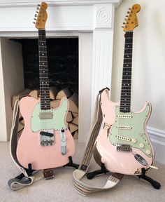 two pink and green guitars sitting next to each other on top of a fireplace mantel