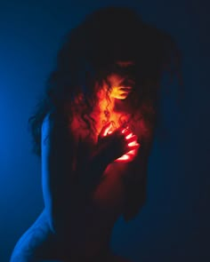 a woman in the dark with her hands on her chest and glowing light behind her