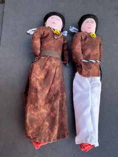 two dolls are laying on the ground next to each other, one is wearing a brown dress