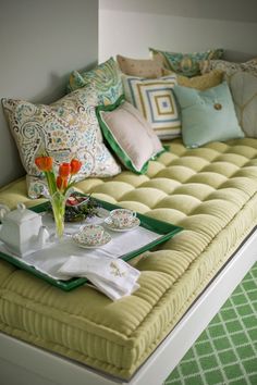 a green and white daybed with flowers on it in a room filled with pillows