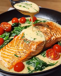 salmon being drizzled with sauce on top of spinach and cherry tomatoes