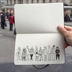 a hand holding an open book with people drawn on it in front of a building