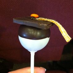 a chocolate graduation cap on top of a candy lollipop with an orange and white stripe