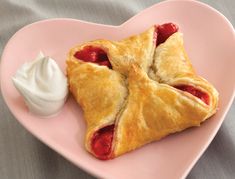 a heart shaped pastry on a pink plate with whipped cream