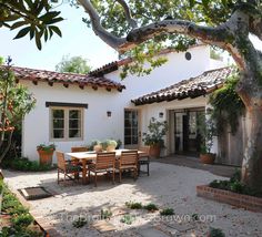 an outdoor patio with table and chairs next to a tree in front of a house