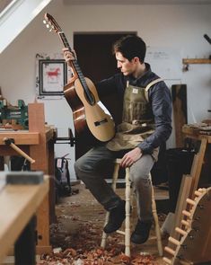 a man sitting on a chair holding a guitar in his hand and looking at the ground