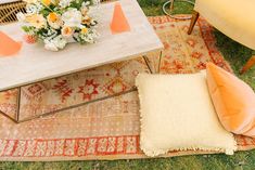 a table with orange and white flowers on it sitting next to a yellow chair in the grass