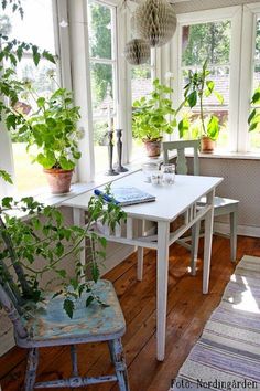 a white table sitting under a window next to a chair and potted plant on top of a wooden floor