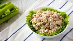 a white bowl filled with chicken salad next to celery stalks on a table