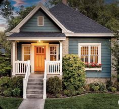 a small blue house with white trim and yellow front door is lit by the evening sun