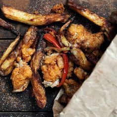 chicken wings and vegetables in a paper bag on a wooden table, with seasoning sprinkles