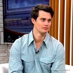 a man sitting on a white chair in front of a tv screen and wearing a blue shirt