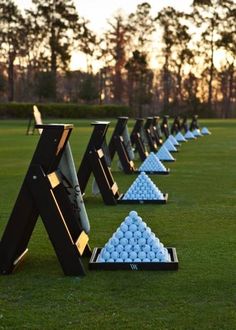 golf balls are lined up in the shape of pyramids on a green field with trees in the background