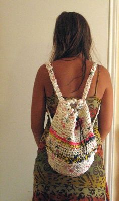 a woman wearing a crochet backpack standing in front of a door with her back to the camera