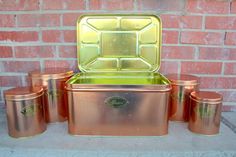 an ice chest with four copper cups in front of it and a brick wall behind it