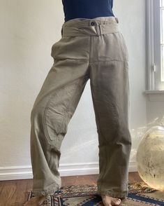 Subdued olive green canvas work pants. Padded legs, front buttons in a sailor style fashion, drop down front with “interior” front pockets, buckle cinch at leg hems and waist. Note: Openings at side “pockets” as these are intended as over pants. See photo. Fabric: CanvasFit: M|L up to 34 inches Measurements (flat): Waist 17 inches (can adjust smaller) Hips 19.5 inches Rise 13.5 inches Inseam 28.5 inches Length 40.5 inches Leg opening 9.75 inches Condition: Excellent Military Style High Waist Parachute Pants In Khaki, Military Style High Waist Khaki Parachute Pants, Khaki High-waisted Utility Parachute Pants, Military Style High-waist Bottoms With Belt Loops, Khaki Utility Work Pants With Belt Loops, Khaki Military Cargo Work Pants, High-waisted Khaki Cargo Pants With Belt Loops, Fitted Khaki Utility Parachute Pants, Khaki Tapered Leg Work Pants With Belt Loops