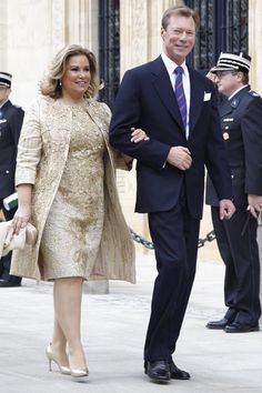 a man and woman are walking down the street in formal attire with other people behind them