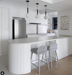 two stools sit at the bar in this modern kitchen with white walls and wood flooring