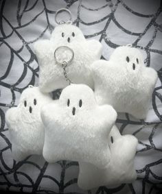 four white plush ghost keychains are on a black and white cloth with spider web