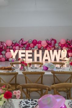 a table set up for a party with pink and silver balloons on the wall behind it