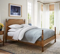 a bed with white sheets and pillows in a bedroom next to a table with flowers on it