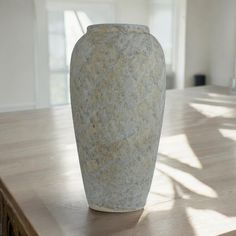 a white vase sitting on top of a wooden table next to a window in a room