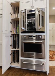 a stainless steel oven and microwave in a white kitchen with wood flooring, built - in shelving