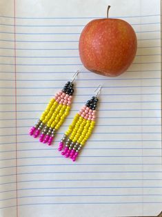 an apple sitting next to two beaded earrings on top of a piece of paper