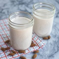 two mason jars filled with almond milk sitting on top of a checkered cloth next to nuts