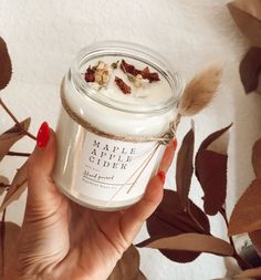 a hand holding a jar of maple apple cider surrounded by autumn leaves and branches