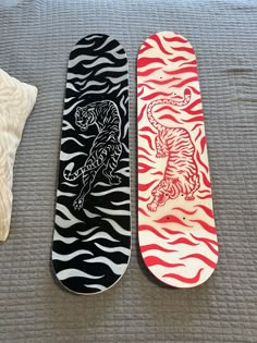 two skateboards sitting on top of a bed next to each other, one with a tiger and the other with zebra stripes